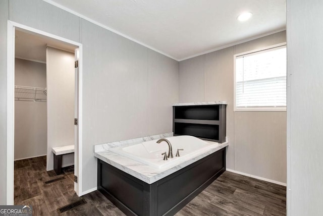 bathroom with a bath, crown molding, a walk in closet, and wood finished floors