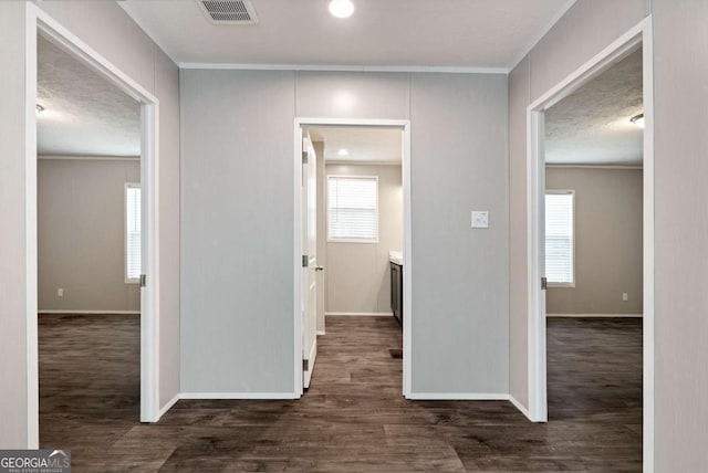 hall with plenty of natural light, visible vents, wood finished floors, and ornamental molding