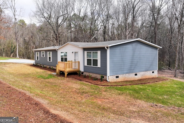 manufactured / mobile home with a front lawn, crawl space, a wooden deck, and a view of trees