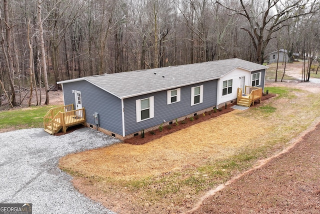 view of front of property featuring driveway, crawl space, roof with shingles, and a view of trees