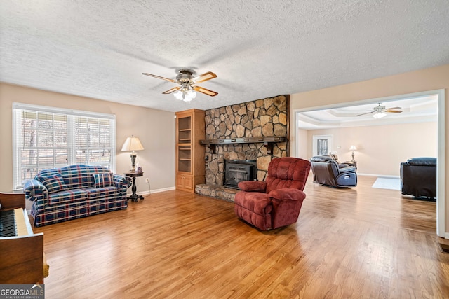 living area with baseboards, ceiling fan, light wood-style flooring, a fireplace, and a textured ceiling