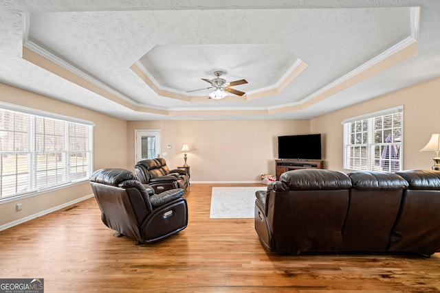 living room featuring light wood-type flooring, a tray ceiling, a healthy amount of sunlight, and a ceiling fan