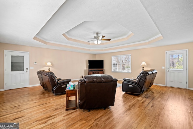 living area featuring light wood finished floors, a raised ceiling, and a ceiling fan