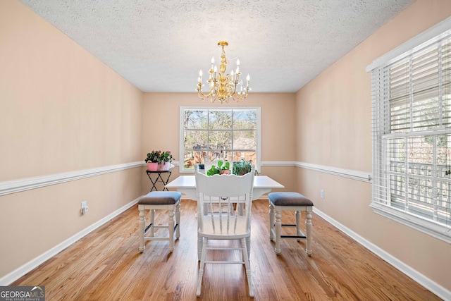 dining area featuring a chandelier, baseboards, a textured ceiling, and wood finished floors