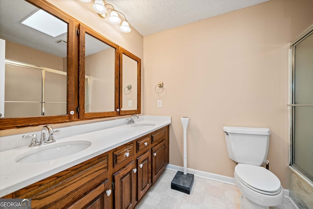 bathroom featuring a shower with door, toilet, double vanity, a textured ceiling, and a sink