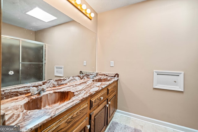 bathroom with a sink, an enclosed shower, baseboards, and a skylight