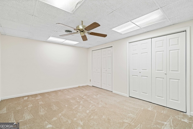 unfurnished bedroom featuring a ceiling fan, baseboards, a drop ceiling, multiple closets, and carpet flooring