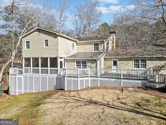 rear view of property featuring a yard, a deck, a chimney, and a sunroom