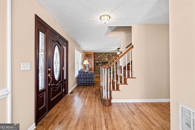 foyer entrance with visible vents, stairway, a textured ceiling, and wood finished floors