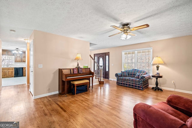 living area with baseboards, stairs, light wood-type flooring, and a ceiling fan