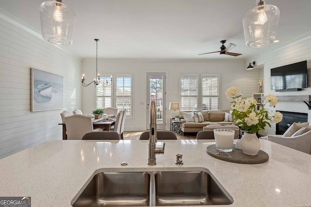kitchen with open floor plan, ceiling fan with notable chandelier, a sink, and light stone countertops