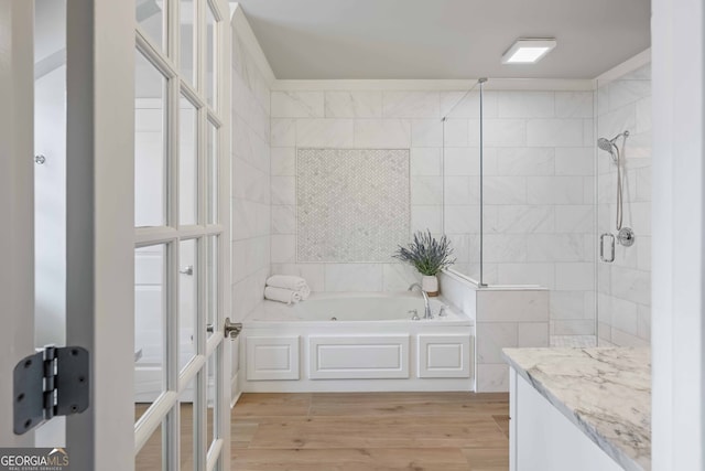 bathroom with a bath, tiled shower, tile walls, and wood finished floors