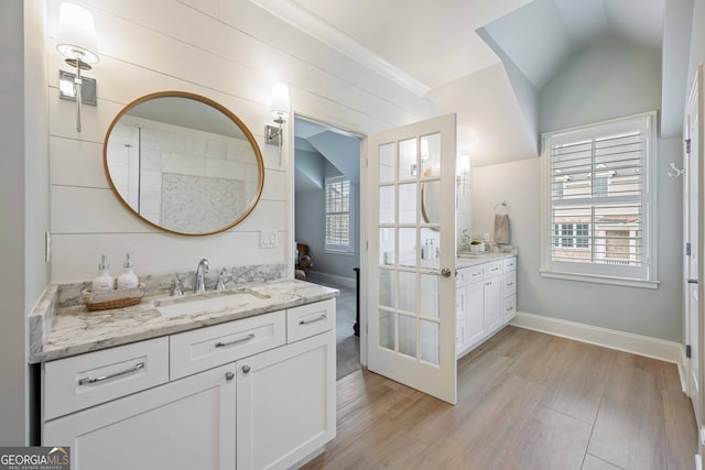 full bath with wood finished floors, baseboards, two vanities, a sink, and vaulted ceiling