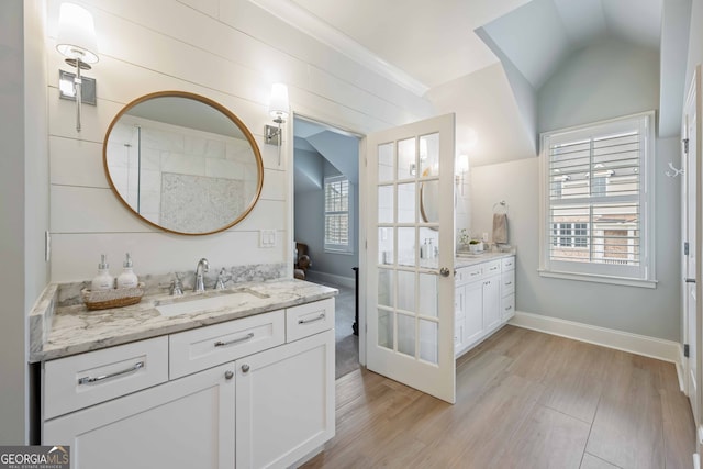 bathroom with two vanities, ornamental molding, wood finished floors, a sink, and lofted ceiling