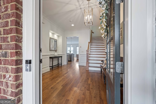 foyer entrance with a notable chandelier, dark wood-style floors, a wainscoted wall, and stairway