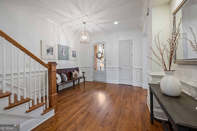 foyer featuring a wainscoted wall, ornamental molding, wood finished floors, stairway, and a decorative wall