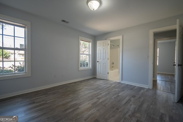 unfurnished bedroom with dark wood-type flooring, visible vents, baseboards, and multiple windows