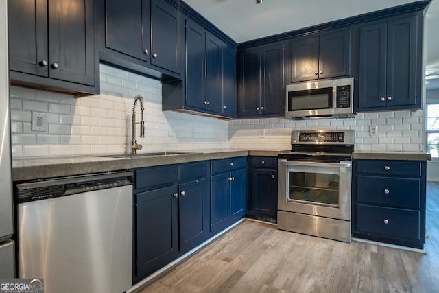 kitchen featuring tasteful backsplash, light wood-style flooring, appliances with stainless steel finishes, blue cabinetry, and a sink