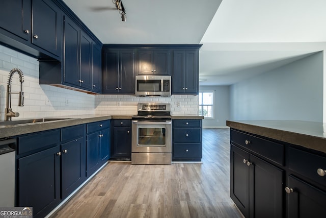 kitchen with blue cabinets, backsplash, stainless steel appliances, and a sink