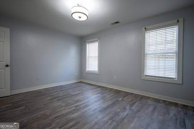 empty room featuring baseboards, visible vents, and dark wood-style flooring