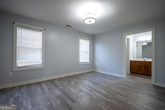 unfurnished bedroom with dark wood-style floors, a sink, ensuite bath, and baseboards