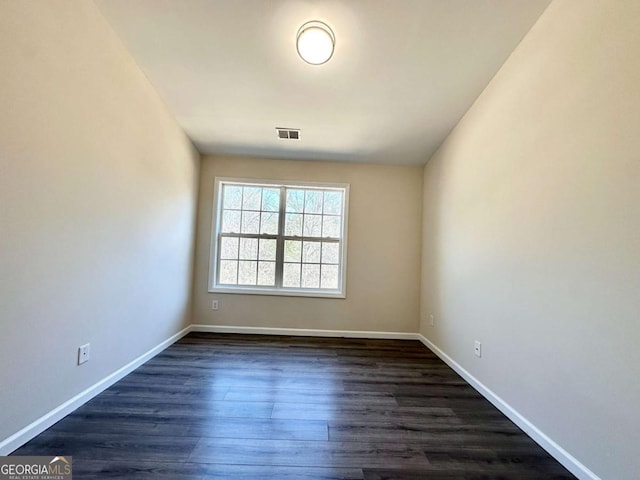 spare room featuring dark wood-type flooring, visible vents, and baseboards