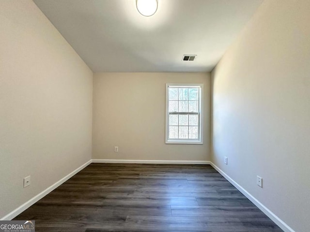 empty room with dark wood-style floors, visible vents, and baseboards