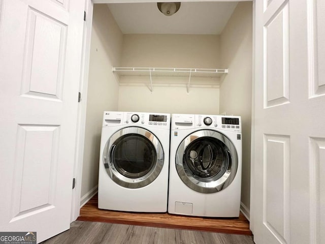 clothes washing area featuring laundry area, baseboards, washer and dryer, and wood finished floors