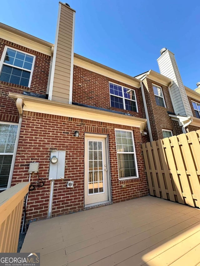 back of property featuring a deck, brick siding, fence, and a chimney