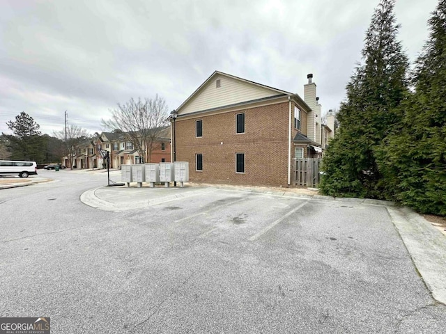 view of property exterior with mail area, a chimney, uncovered parking, and brick siding