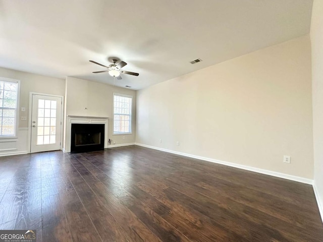 unfurnished living room featuring ceiling fan, a fireplace, dark wood finished floors, and baseboards