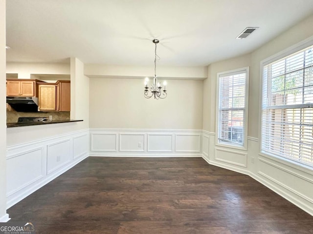 unfurnished dining area featuring a wainscoted wall, dark wood finished floors, visible vents, a decorative wall, and an inviting chandelier