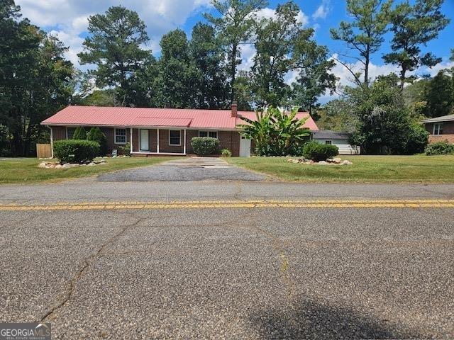 view of front of property featuring brick siding, driveway, a chimney, and a front lawn