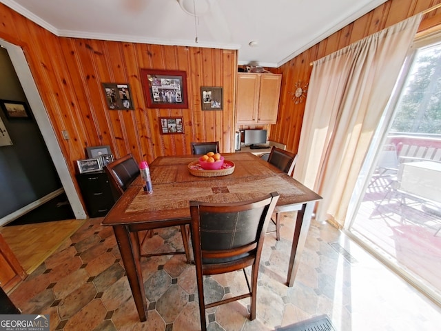 dining area featuring stone finish flooring, crown molding, and wooden walls