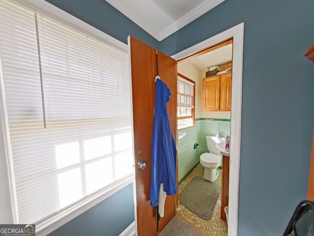 bathroom featuring wainscoting, crown molding, tile walls, and toilet