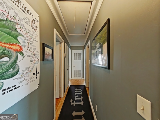 hall with attic access, visible vents, baseboards, ornamental molding, and light wood-type flooring