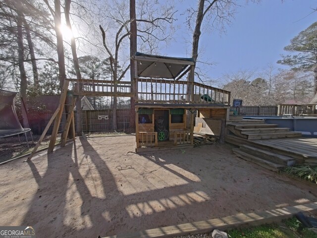 back of house with a trampoline, a playground, a patio, fence, and a wooden deck