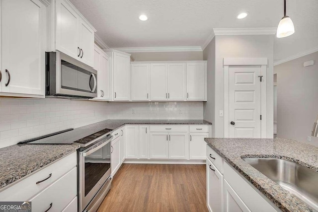 kitchen featuring a sink, white cabinets, appliances with stainless steel finishes, ornamental molding, and light wood finished floors