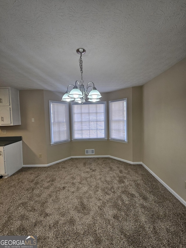 unfurnished dining area with baseboards, visible vents, an inviting chandelier, a textured ceiling, and carpet floors