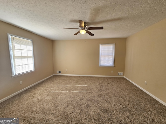 carpeted spare room featuring a wealth of natural light, a ceiling fan, visible vents, and baseboards