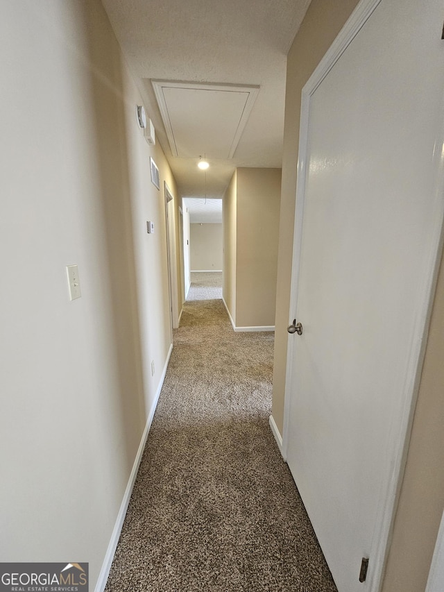 hallway featuring carpet, attic access, and baseboards