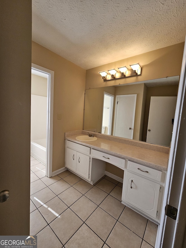 full bath with a textured ceiling, tile patterned flooring, vanity, and baseboards