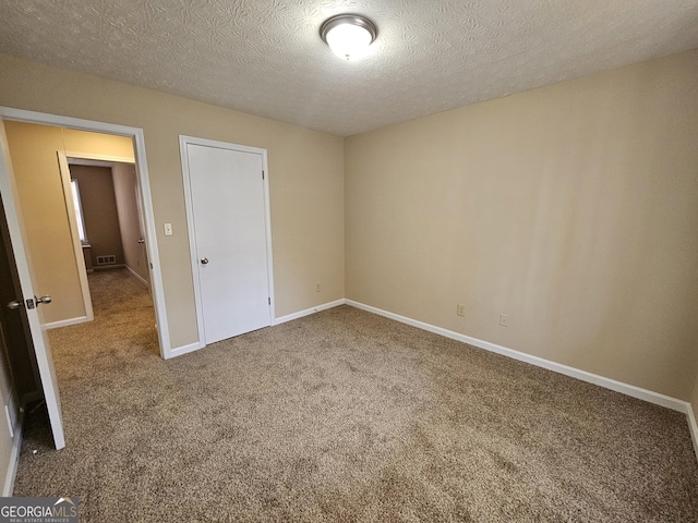 unfurnished bedroom featuring a textured ceiling, carpet floors, visible vents, and baseboards