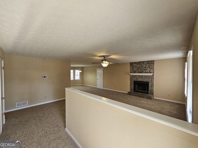 hall with a textured ceiling, dark colored carpet, visible vents, and baseboards