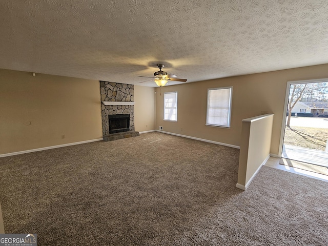 unfurnished living room with carpet floors, ceiling fan, baseboards, and a stone fireplace