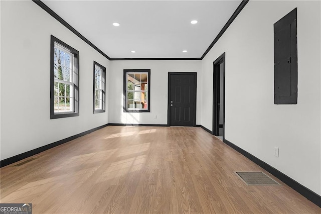 empty room featuring crown molding, visible vents, light wood-style floors, electric panel, and baseboards