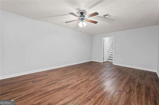 empty room featuring visible vents, dark wood-type flooring, a textured ceiling, baseboards, and stairs