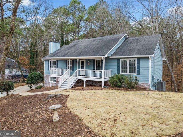 ranch-style home with a shingled roof, cooling unit, covered porch, and a chimney