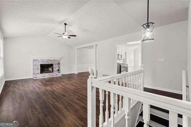 unfurnished living room with a textured ceiling, wood finished floors, a ceiling fan, vaulted ceiling, and a brick fireplace