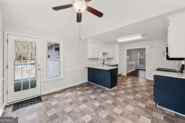 kitchen featuring light countertops, white cabinetry, range, a peninsula, and baseboards